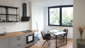 Een moderne keuken met een houten aanrechtblad, inbouwplanken, een zwarte afzuigkap en een zithoek met een tafel en stoelen.