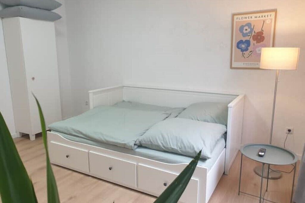A bedroom with a bed, bedside table, and a wall-mounted lamp.