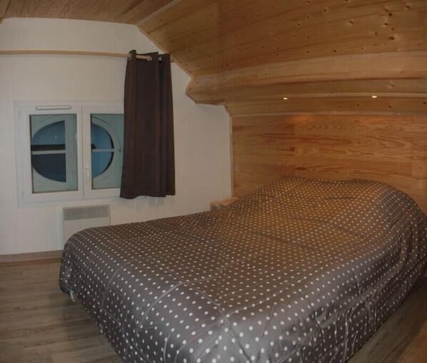 A bedroom with a bed, a window with curtains, and a wooden ceiling. - Villa Primevere N°3 (Mont-Dore)