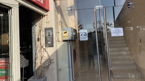 Entrada de un edificio con puerta de vidrio, letrero rojo para bar y parrilla, y señal de circuito cerrado de televisión.