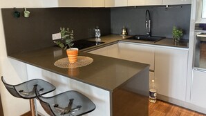 Una cocina moderna con una isla central, muebles de cocina blancos y negros, y una pequeña barra con taburetes.