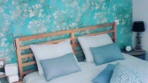 Ein Schlafzimmer mit einem hölzernen Kopfteil, einem Bett mit weißer und blauer Bettwäsche und einer Wand mit blaugrünem Muster.