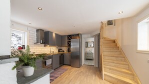 Een moderne keuken met grijze kastjes, een roestvrijstalen koelkast en een houten trap naar een badkamer.