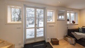 Een moderne woonkamer met een grote glazen deur die uitkomt op een besneeid gebied, een donkere bank en een kleine houten tafel.