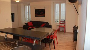 A compact living space with a kitchenette, dining area, and a sofa with red cushions.