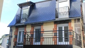 A two-story building with a blue tiled roof, brick and stone facade, and black metal balconies.