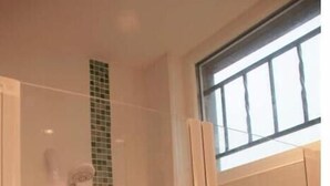 A shower area with a glass door, a green-tiled accent wall, and a window above.