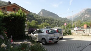Ein Parkplatz mit zwei Autos, ein Gebäude mit Schrägdach und Berge im Hintergrund.