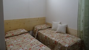 Ein kleiner, schlichter Raum mit zwei Betten, einem Holz-Kopfteil und einer Wandleuchte.