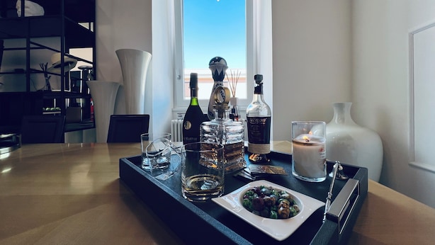 Een eettafel met een dienblad waarop een fles Martini-wijn, een fles Jack Daniel's-whiskey, een glas, een kaars en een schaal met olijven staan.