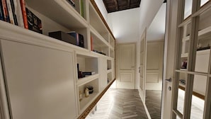 Een gang met een visgraatvloer, witte muren en een boekenkast vol boeken en decoratieve objecten.