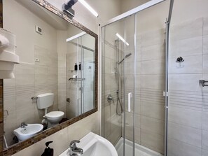Ein modernes Badezimmer mit einer Duschkabine, einem weißen Waschbecken und einem Bidet.