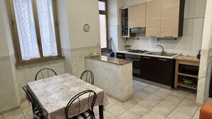 A compact kitchen with a dining area, featuring a small island, a stove, and cabinets. - Casa Vacanze Il Conservatorio - by Be Your Home (Civitavecchia)
