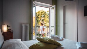 Een hotelkamer met een bed, een nachtkastje, een raam met uitzicht op een balkon en een radiator.