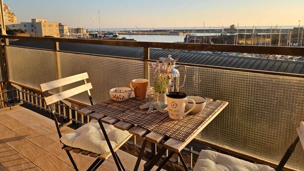 Een balkon met een tafel voor twee personen, met uitzicht op een jachthaven met boten en gebouwen.