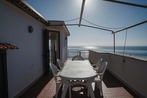 An outdoor patio with a table and chairs, a view of the sea, and a building entrance. - Holiday Apartment by the sea (Santa Marinella)