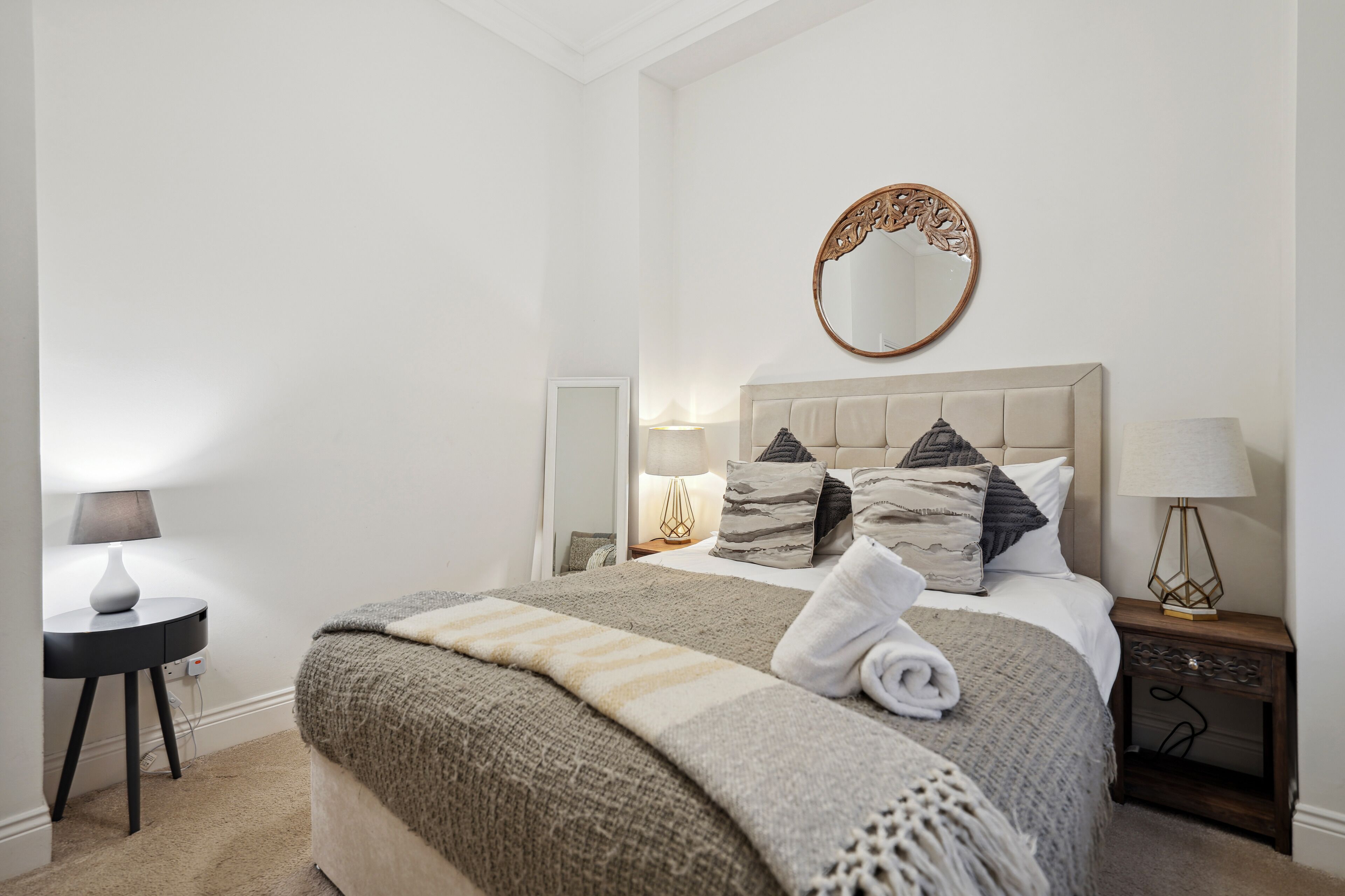 Ein Schlafzimmer mit einem Bett, zwei Nachttischen, einem Spiegel und einer Lampe.