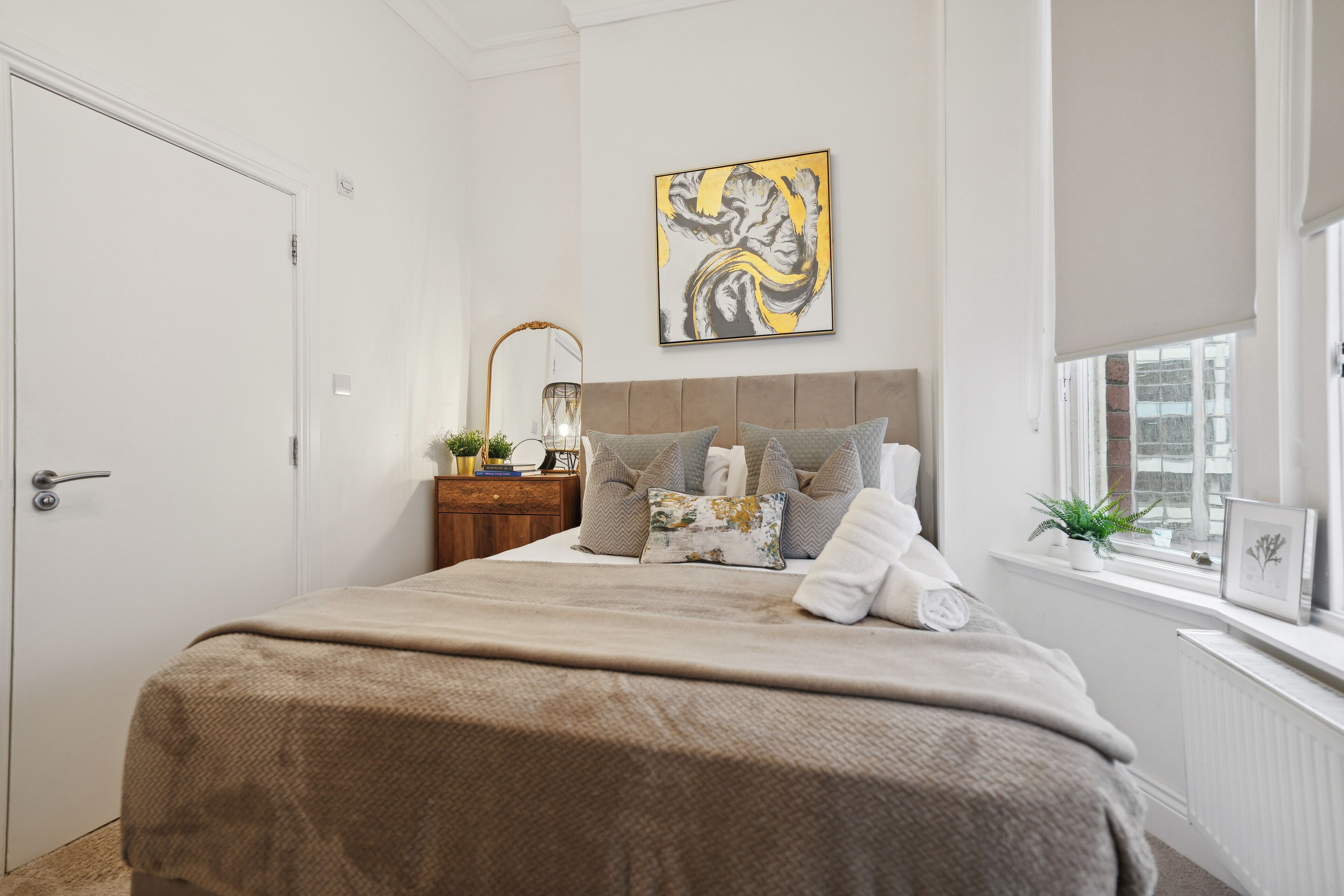 A bedroom with a bed, a bedside table, a lamp, a window, and a wall art piece.