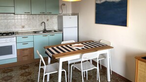 A kitchen with teal cabinets, a white refrigerator, a striped table, and a painting of a wave on the wall. - Casa Raffaello - by Be Your Home (Santa Marinella)