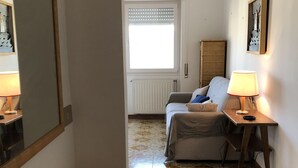 A hotel room with a wooden desk, a fish-shaped decoration, a bed with a blue and beige blanket, a standing lamp, and a window with blinds. - Casa Raffaello - by Be Your Home (Santa Marinella)