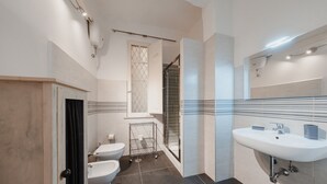 Een moderne badkamer met een witte wastafel, twee toiletten, een douche en een handdoekhouder.