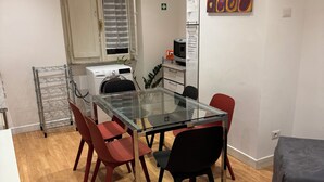 Een functionele keuken met een wasmachine, een kleine koelkast en een eettafel met stoelen.