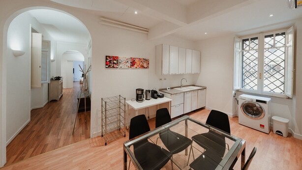 Een moderne keuken met witte kasten, een eethoek met een glazen tafel en een wasruimte met een wasmachine.