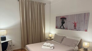 A neatly made bed with a folded towel, a bedside lamp, and a wall art piece depicting two figures. - Mazzini 144 -Stanza 1(Bagno Esterno) byBeYourHome (Rome)