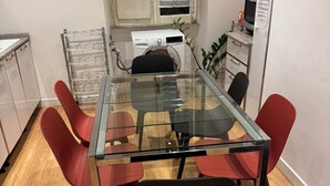 Un comedor moderno con una mesa de vidrio rodeada de sillas rojas, una lavadora y una pequeña zona de cocina con fregadero y encimera.