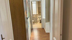 Un pasillo con suelo de madera que conduce a un baño con ventana y lavabo.