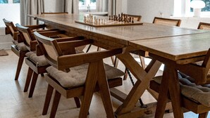 A dining room with a long wooden table and chairs, a chessboard, and large windows with curtains. - De Wever Lodge (Otterlo)