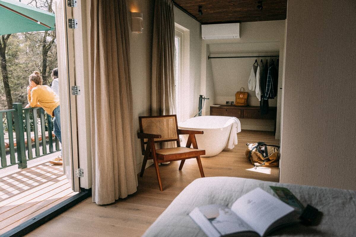 Ein Zimmer mit Holzboden, einem Sessel, einem Tisch, einem Bett und einem Fenster.