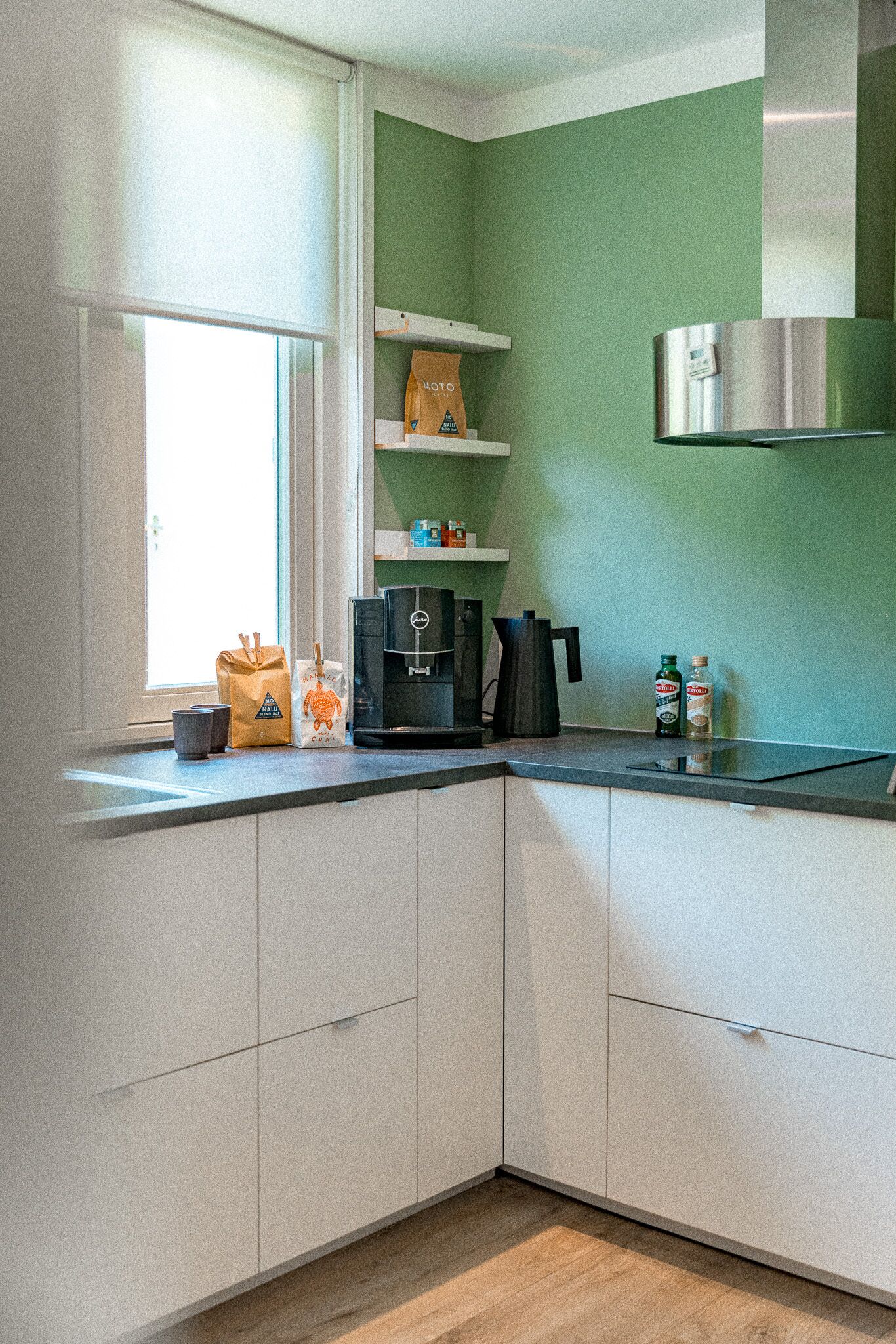 A kitchen with white cabinets, a green wall, a window, and a stainless steel range hood.