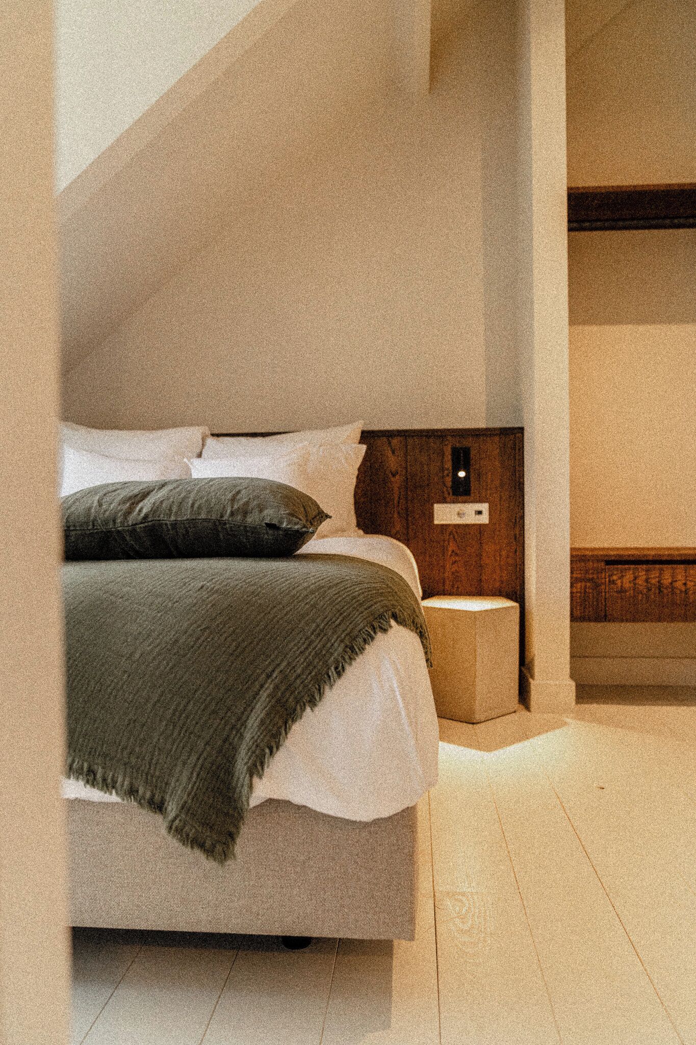 A bedroom with a bed, pillows, a nightstand, and a wooden headboard.
