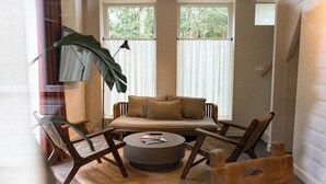 A cozy living room with a sofa, chairs, a coffee table, and a large plant. - De Wever Lodge (Otterlo)