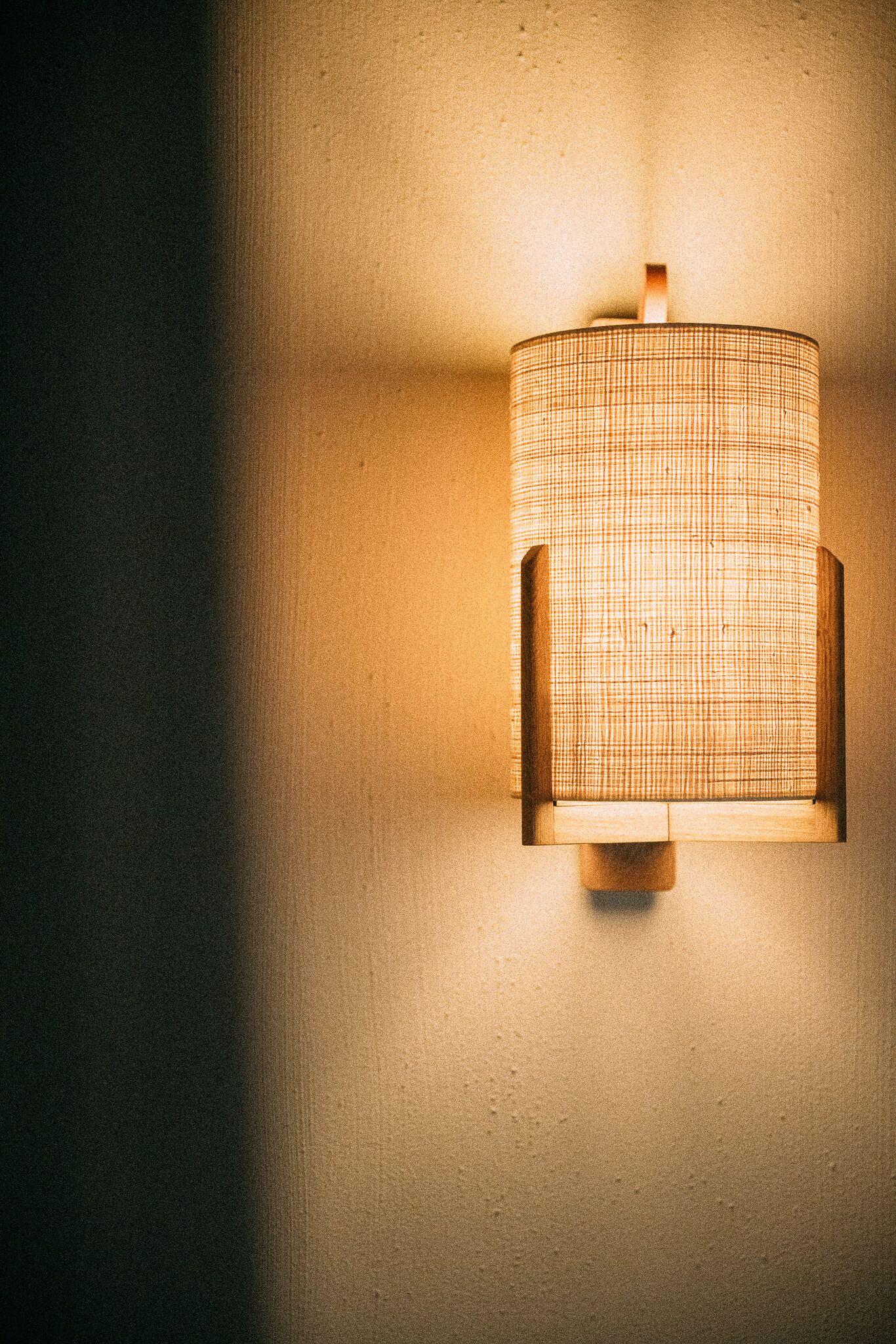 Une lampe murale dotée d’un abat-jour en tissu tressé.