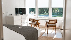 A bedroom with a bed, a desk, and a TV. There are windows with a view of greenery. - De Wever Lodge (Otterlo)