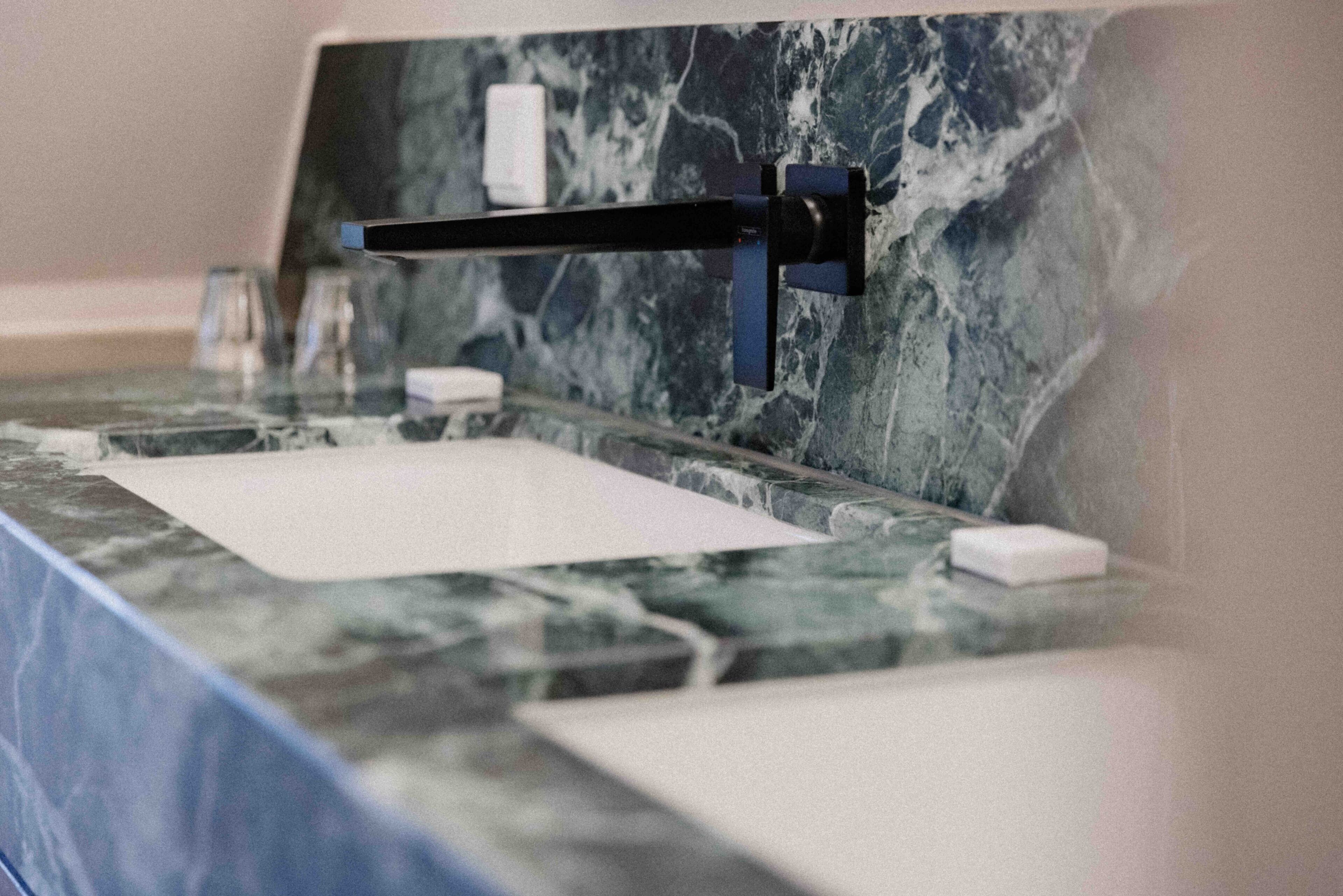 A bathroom with a marble countertop, a black towel rack, and a white soap dish.