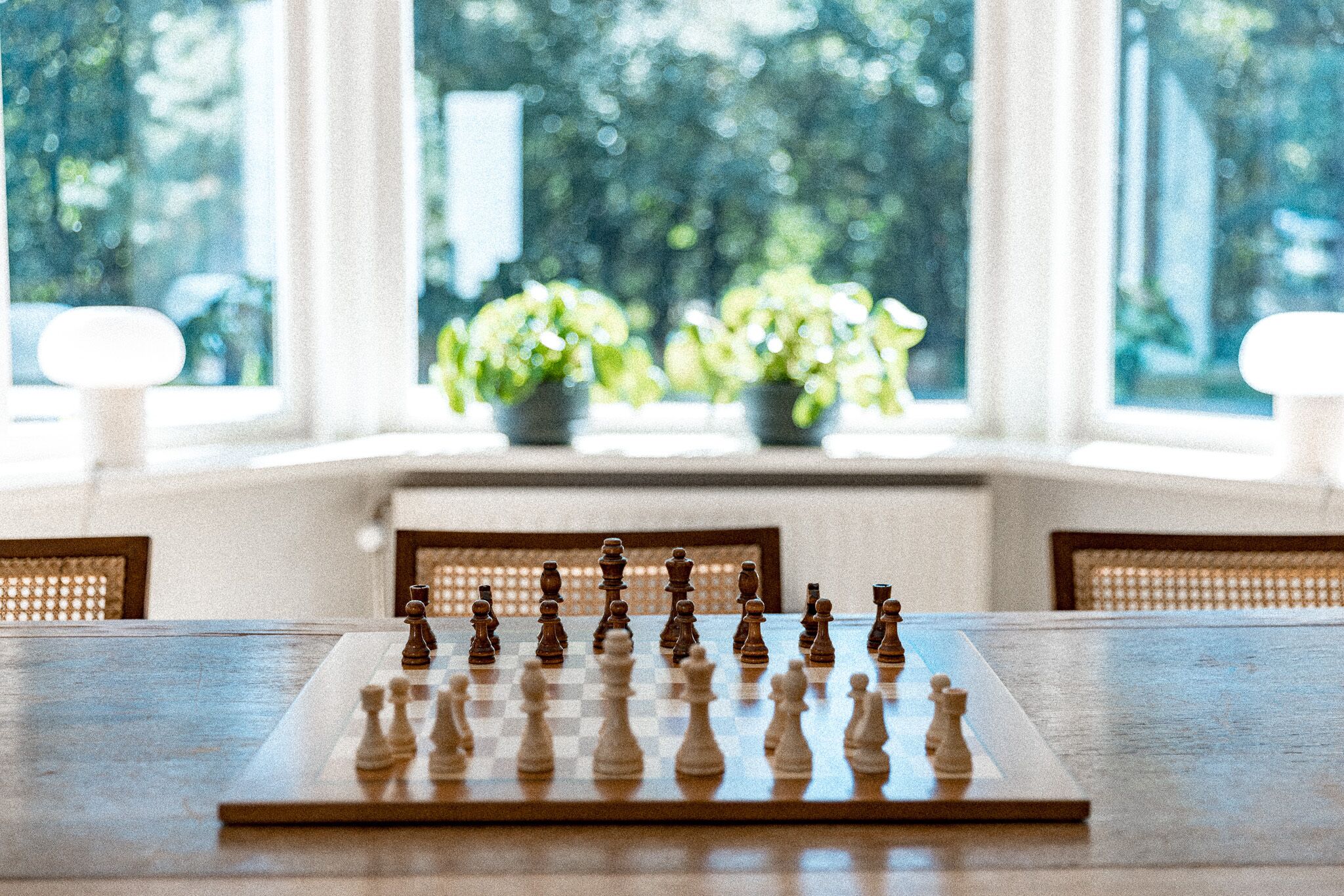 A chessboard on a table with a view of greenery through large windows.