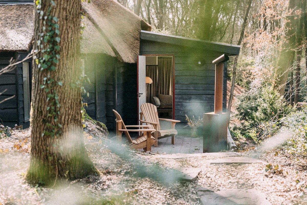 Eine rustikale Holzhütte mit einem strohgedeckten Dach, Holzstühlen und einer kleinen Veranda.