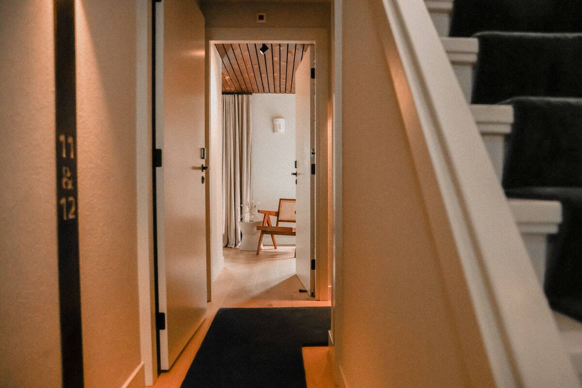 Ein Flur, der zu einem Raum mit Stuhl und Tisch führt, mit einer Tür mit einer Nummer und einer Treppe.