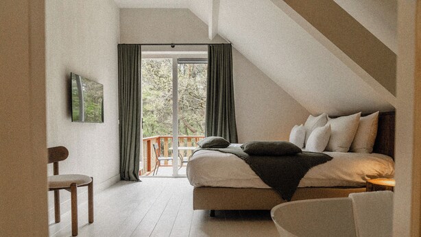 A bedroom with a bed, a chair, and a view of the outdoors through a large window. - De Wever Lodge (Otterlo)