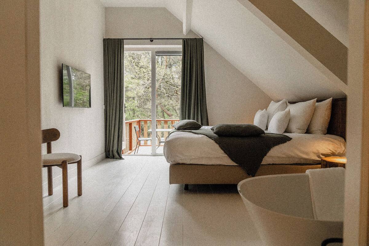 Ein Schlafzimmer mit Bett, Stuhl und Blick ins Freie durch ein großes Fenster.