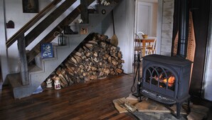 Een rustiek interieur met een houten trap, een stapel hout, een oude fornuis en een deur naar een andere kamer.