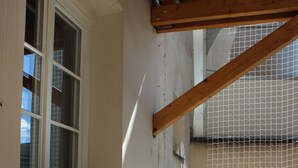 Ein Balkon mit weißem Metallstuhl, einem kleinen runden Tisch und einem Fenster mit weißem Rahmen.