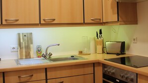 Eine kleine Küche mit Holzausstattung, einem Edelstahl-Spülbecken, einem Toaster und einem Einbauofen.