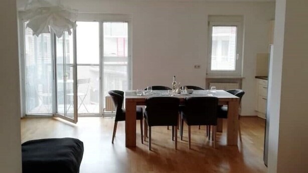 Comedor con mesa y sillas de madera, ventanas amplias y vistas al exterior.