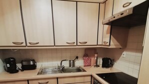 A compact kitchen with light wood cabinets, a stainless steel sink, a black stove, and a coffee maker.