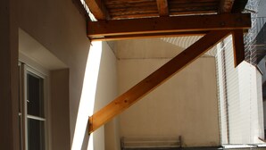 A wooden deck with a table and chairs, a window, and a balcony railing.