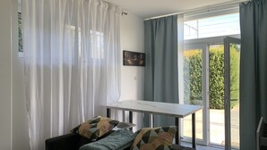 A modern living room with a sofa, a small table, and a view of a green landscape through the glass door. - Appartement Séparé Avec Parking Gratuit (Vilvoorde)